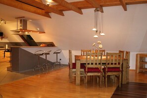 A dining area with a wooden table and chairs, a kitchen in the background, and pendant lighting. - Holiday apartment with 3 bedrooms (Wangerland)