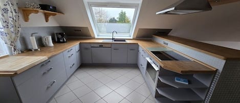 Eine kleine Küche mit grauen Schränken, einer Holz Arbeitsplatte, einem eingebauten Backofen und einem Fenster über der Spüle.