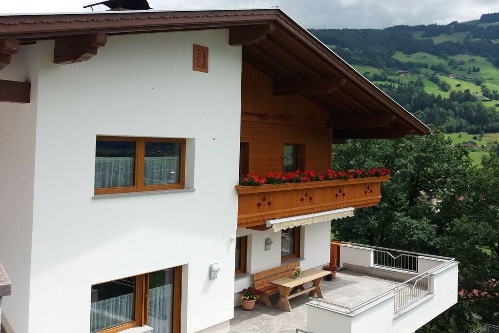 Ein zweistöckiges Gebäude mit einem Balkon, Holzgeländern und Blick auf grüne Hügel.