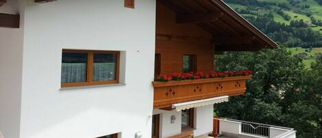 Ein zweistöckiges Gebäude mit einem Balkon, Holzgeländern und Blick auf grüne Hügel.