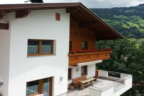 Een gebouw met twee verdiepingen, een balkon, houten hekwerk en uitzicht op groene heuvels.