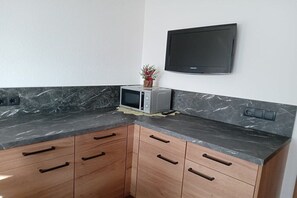 A kitchen with a marble countertop, wooden cabinets, a microwave, and a wall-mounted television. - Hippach Sporer family (Hippach)