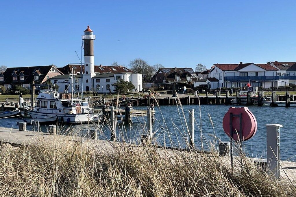 A harbor with a lighthouse, boats, and houses along the waterfront.
