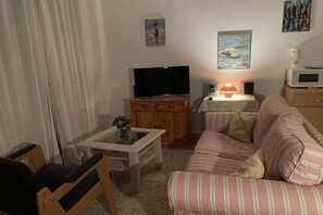 Un saló amb televisió, una taula de cafè amb un ram, un sofà i una làmpada.