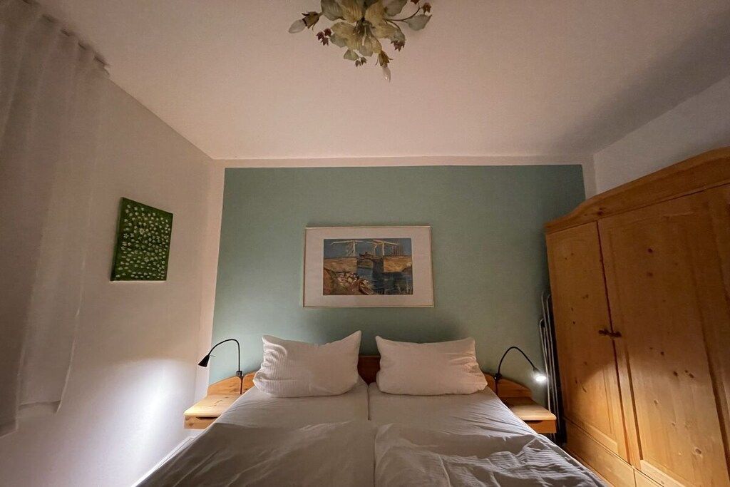 Un dormitorio con cama, armario de madera, un cuadro en la pared y una lámpara en el techo.