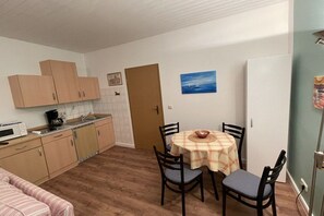 A compact kitchen with wooden cabinets, a microwave, and a dining table with chairs. - Holiday apartment with 1 bedroom (Timmendorf-Strand, Insel Poel)