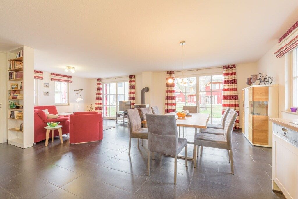 A spacious living area with a dining table, red and white curtains, and a view of the outside.