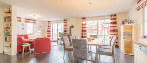 A spacious living area with a dining table, red and white curtains, and a view of the outside.