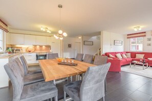 Eine moderne Küche mit weißen Schränken, einem Holztisch im Essbereich und einem roten Sofa im Wohnzimmer.