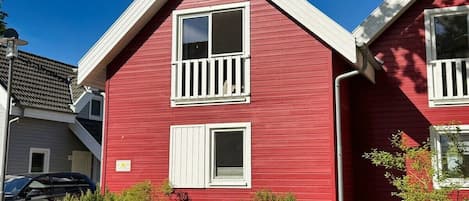 Une maison rouge à deux étages, dotée d’un balcon blanc, d’un garage et d’une allée.