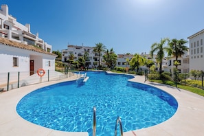 A swimming pool with a curved edge, surrounded by a fence, and adjacent to a building with balconies. - Finca San Antonio Mijas II – Sea View Apartment with Pool & Terrace in Mijas Pueblo (Mijas Pueblo)
