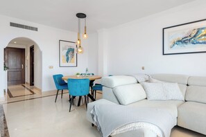 A modern living room with a sofa, chairs, a dining table, and artwork. - Finca San Antonio Mijas II – Sea View Apartment with Pool & Terrace in Mijas Pueblo (Mijas Pueblo)