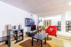 Ein Wohnzimmer mit Flachbildfernseher, Bücherregal, einem roten Sessel und einer Couch.