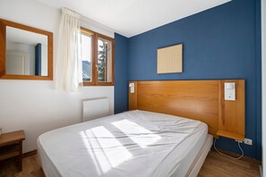 A bedroom with a single bed, a window with curtains, a wooden headboard, a bedside table, and a wall-mounted light switch. - Apartment 'Albiez 4 to 6 guests' with mountain view and balcony (Albiez-Montrond)