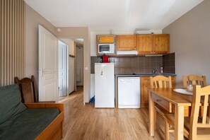 A compact kitchen with wooden cabinets, a microwave, a refrigerator, and a dishwasher. There is a dining table with chairs and a sofa in the adjacent living area. - Apartment 'Albiez 4 to 6 guests' with mountain view and balcony (Albiez-Montrond)