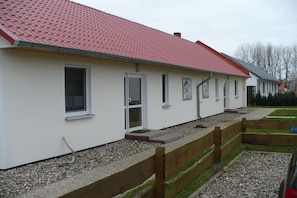 A row of single-story buildings with a red-tiled roof, white walls, and a gravel pathway leading to the entrance. - Holiday apartment in Glowe with swimming pool (Glowe)