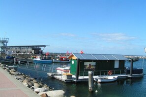 A marina with boats docked, a small building with a metal roof, and a rocky shoreline. - Holiday apartment in Glowe with swimming pool (Glowe)
