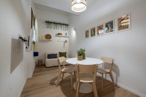 Ein Essbereich mit einem runden Tisch, vier Stühlen, einer hängenden Lampe und Wandregalen mit Dekorationsobjekten.