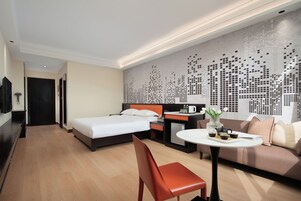 Habitación de hotel con cama, escritorio, silla, sofá, una mesita con un florero y un adorno en la pared.