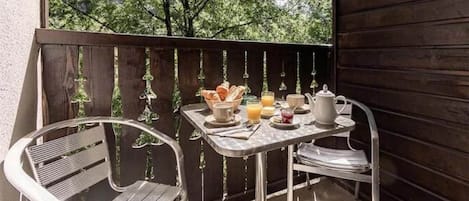 Un balcón con una mesa dispuesta para el desayuno, con cruasanes, jugo y una tetera.