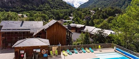 A pool area with a wooden building, a lifebuoy, and a mountain backdrop.