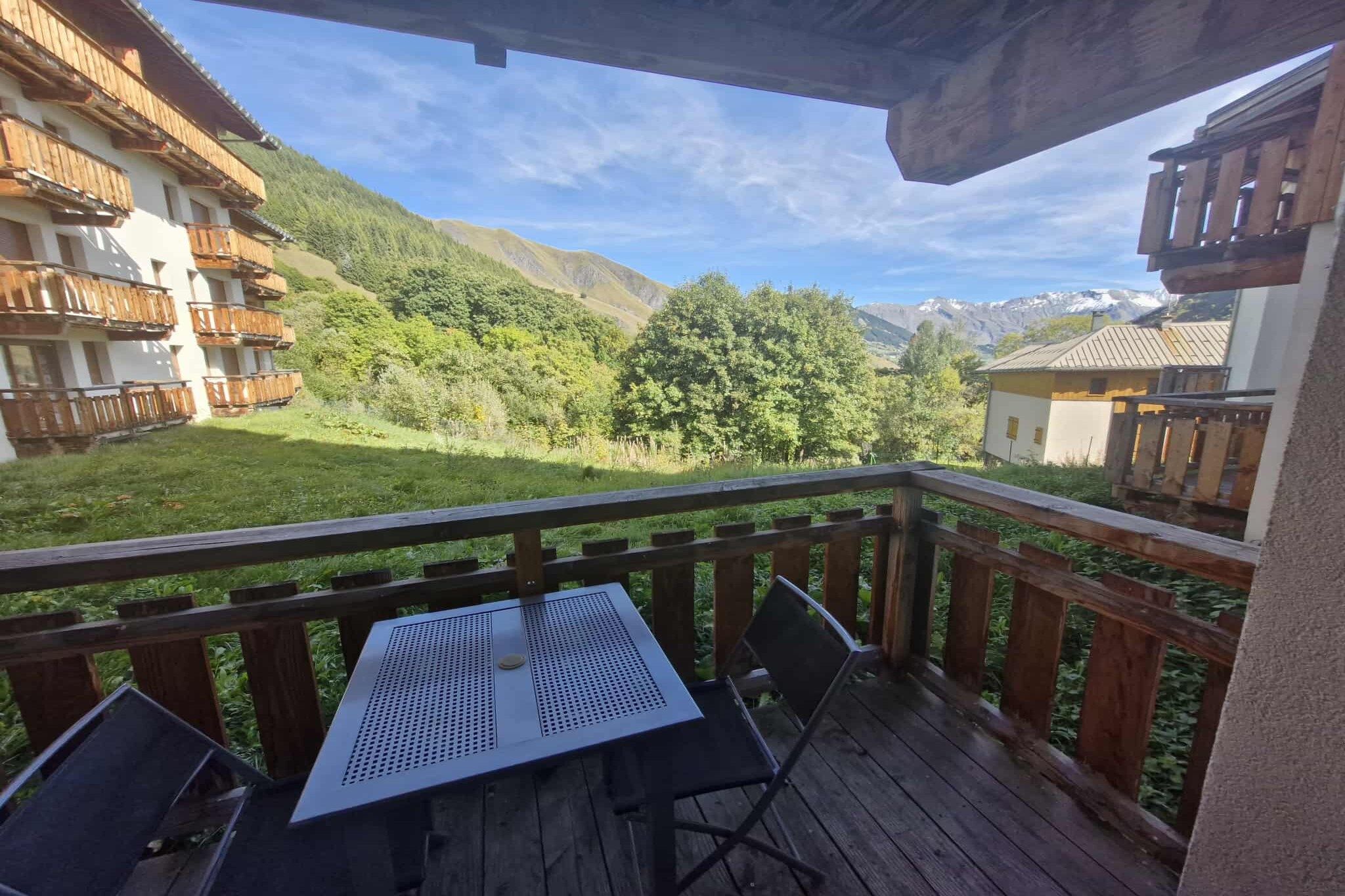 A wooden deck with a table and chairs, overlooking a mountainous landscape with buildings in the background.