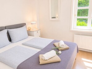 A neatly made bed with pillows and a folded towel, a bedside table with a lamp, and a window with a view of greenery. - Haus Schneekappe - 190qm beste Lage (Winterberg)