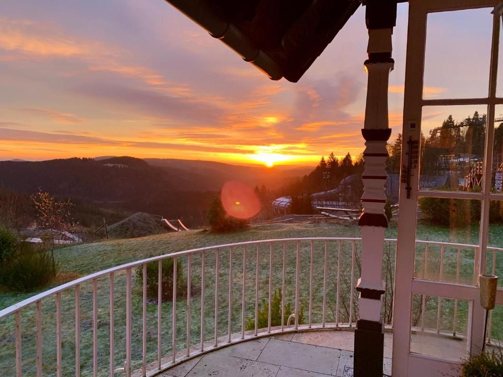 En balkon med udsigt over en solnedgang over et bakket landskab.