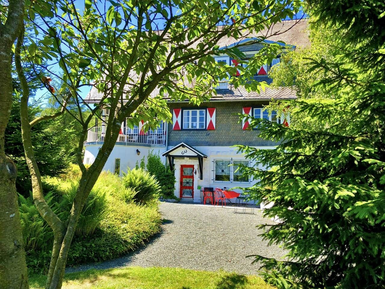 A building with a red door, a balcony, and a gravel path leading to the entrance.