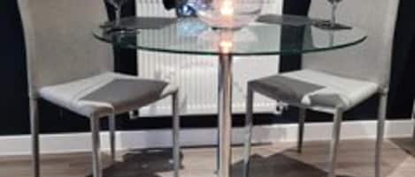 A modern dining table with a glass top and metal base, surrounded by two chairs with cushioned seats.