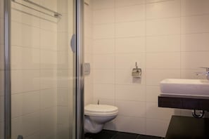 Ein Badezimmer mit Duschkabine aus Glas, einer weißen Toilette und einem Waschbecken mit dunkler Arbeitsplatte.