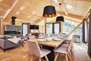A spacious living area with a fireplace, a dining table set for six, and a large window offering a view of the outdoors.