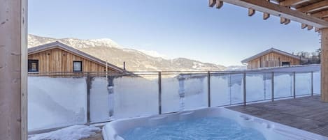 Ein Whirlpool unter einer Holzpergola mit Blick auf schneebedeckte Berge.