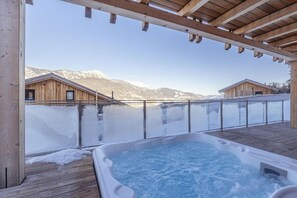 A hot tub under a wooden pergola with a view of snow-covered mountains.