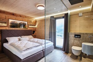 A modern bedroom with a bed, a large window, and a bathroom with a sink and toilet.