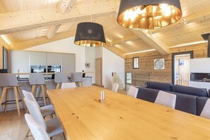 Ein modernes Interieur mit Holzboden, einem Essbereich mit langem Tisch und Stühlen sowie einer Küche im Hintergrund.