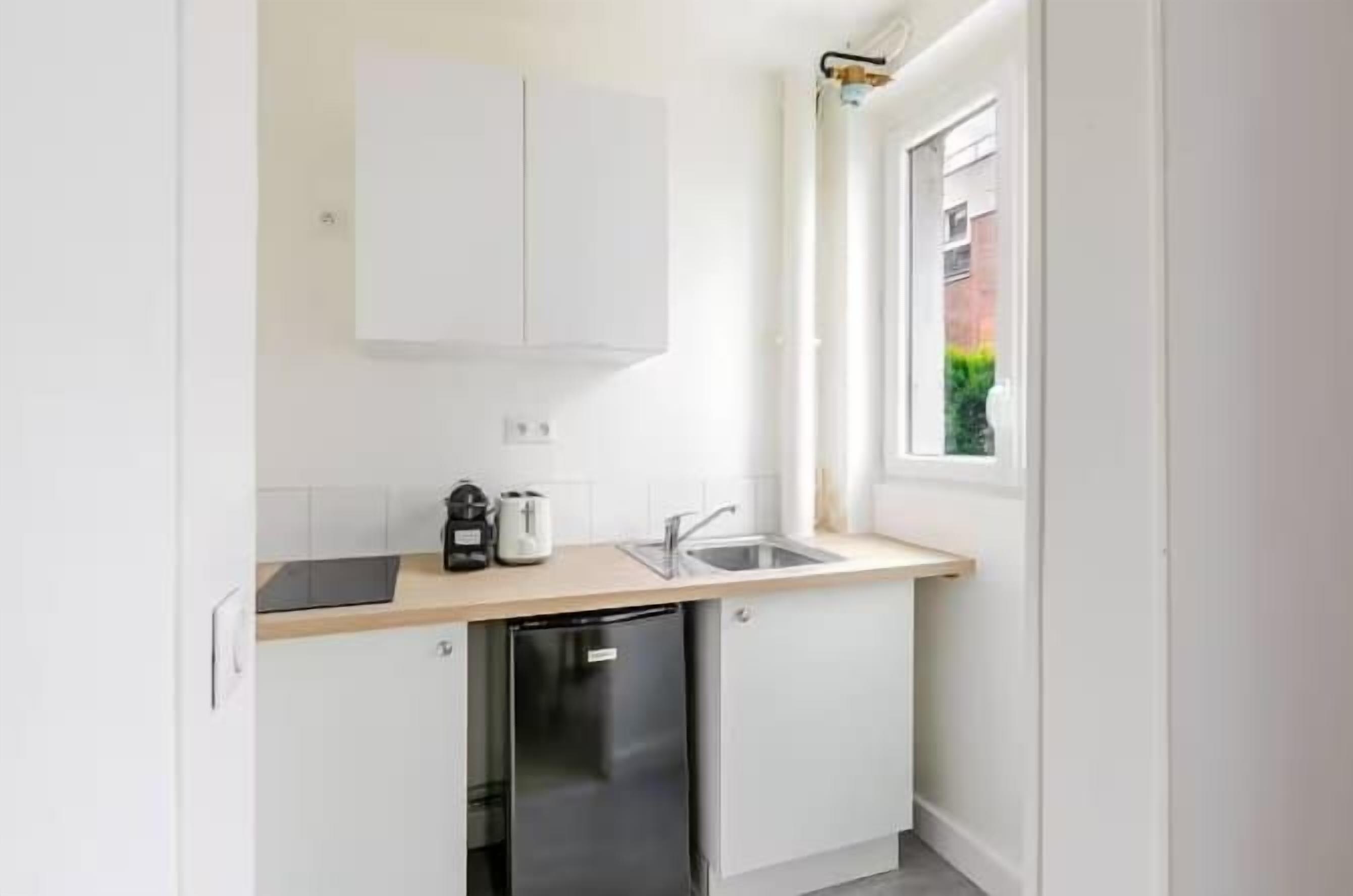 Una cocina compacta con alacenas blancas, lavavajillas y ventana que proporciona luz natural.