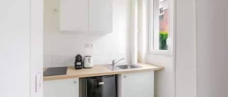 Una cocina compacta con alacenas blancas, lavavajillas y ventana que proporciona luz natural.
