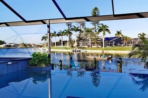 Une piscine à débordement offrant une vue sur un lac et des palmiers, une jetée avec des chaises, et un ciel dégagé.