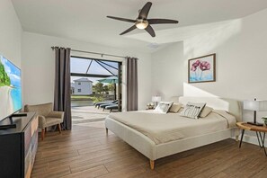 Une chambre à coucher comprenant un lit, un bureau, une chaise, un ventilateur de plafond et une vue sur l’extérieur.