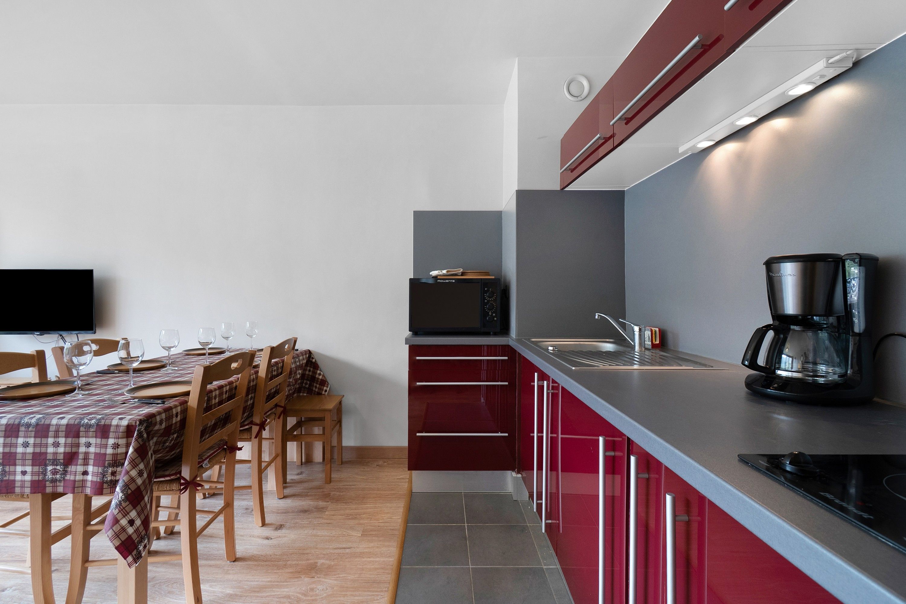 Een moderne keuken met rode kastjes, een zwarte magnetron en een koffiezetapparaat.