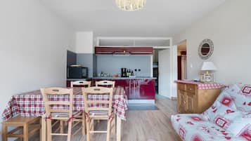 Un espace de vie compact comprenant un coin repas, une kitchenette et un canapé agrémenté d’un ensemble de literie à motifs.