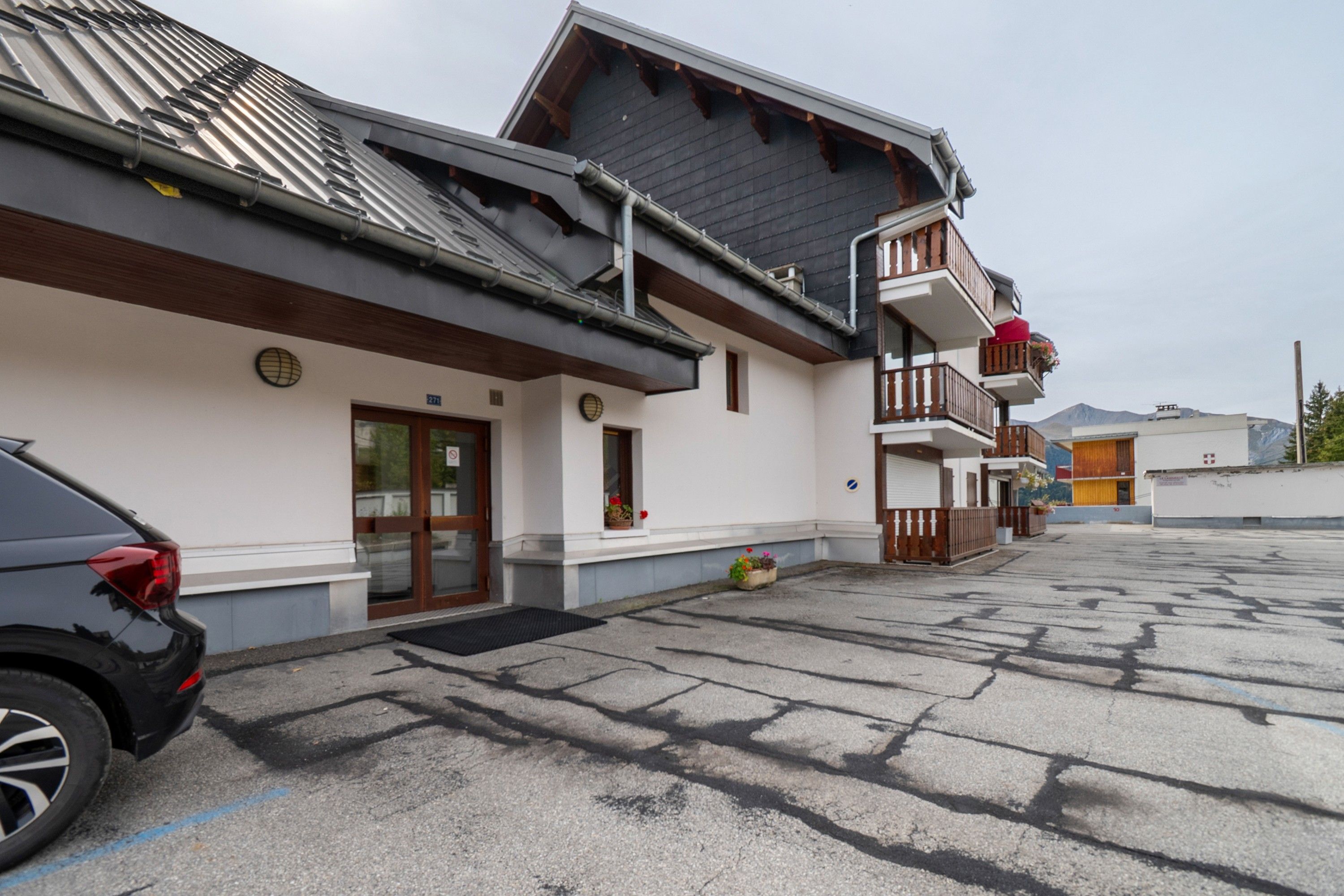 A building with a sloped roof, a wooden balcony, and a car parked in front.