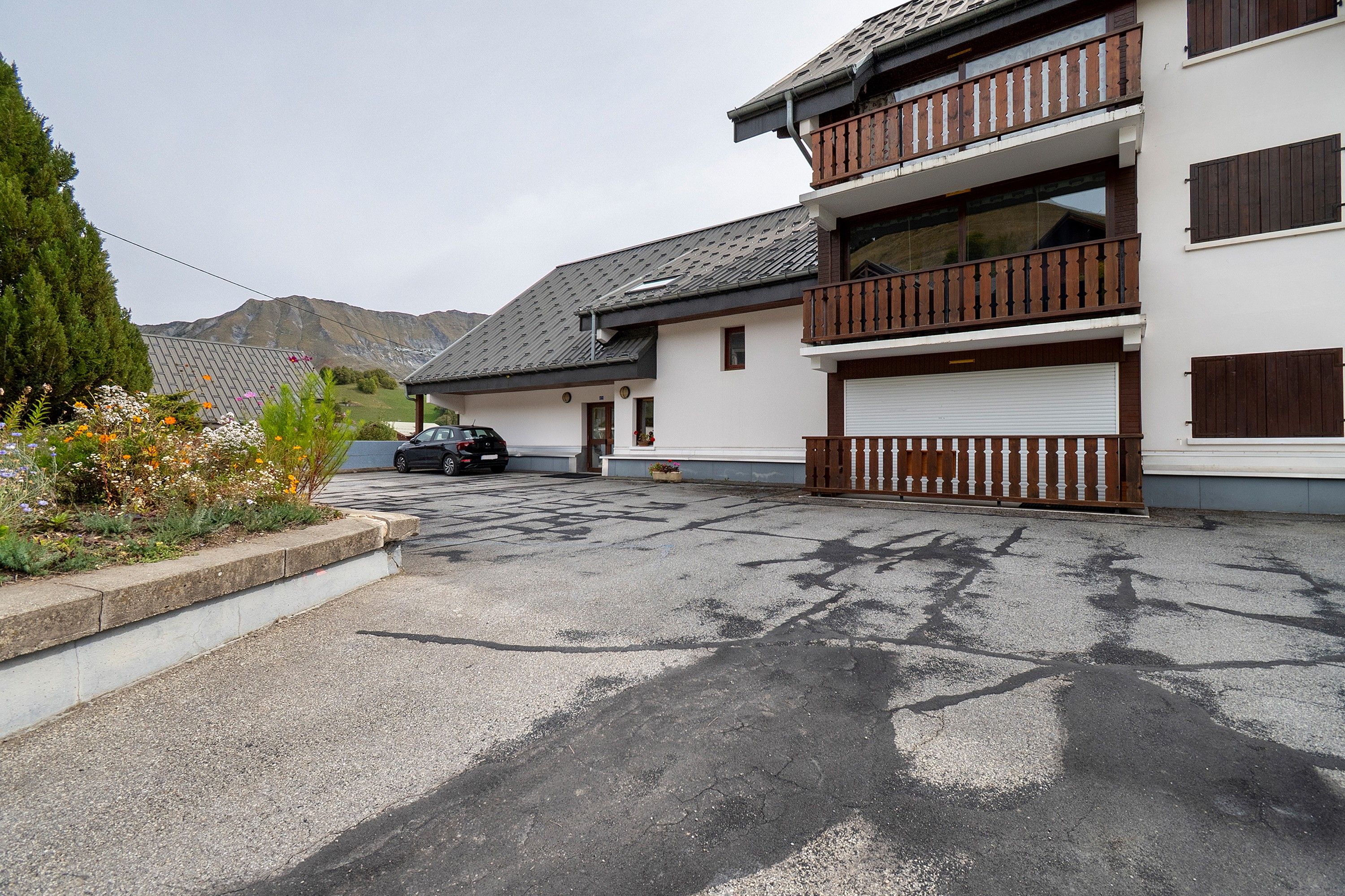 Un bâtiment à deux étages avec une porte de garage, une voiture garée devant et une montagne en arrière-plan.