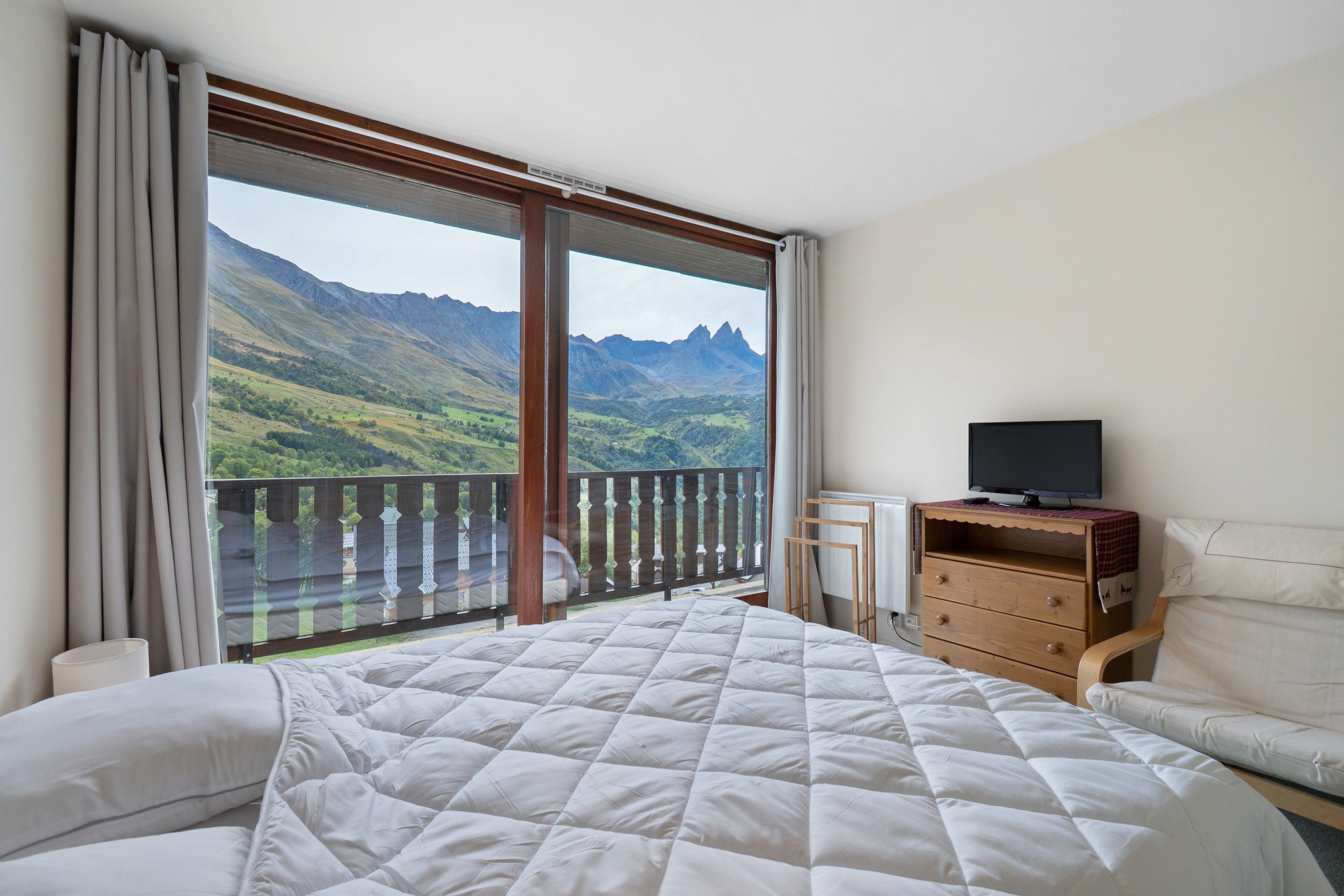 Une chambre avec un grand lit, un téléviseur posé sur une commode en bois et un balcon offrant une vue sur la montagne.