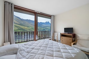 Een slaapkamer met een groot bed, een televisie op een houten dressoir en een balkon met uitzicht op de bergen.