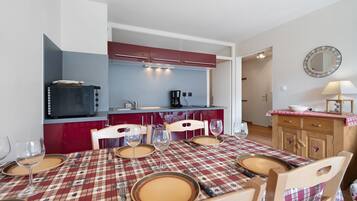 A dining area with a red and white checkered tablecloth, wooden chairs, and a kitchen in the background.