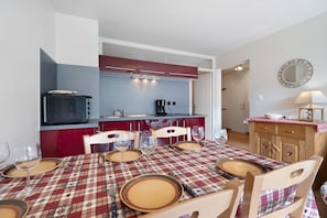 Een eethoek met een rood-wit geruit tafelkleed, houten stoelen en een keuken op de achtergrond.