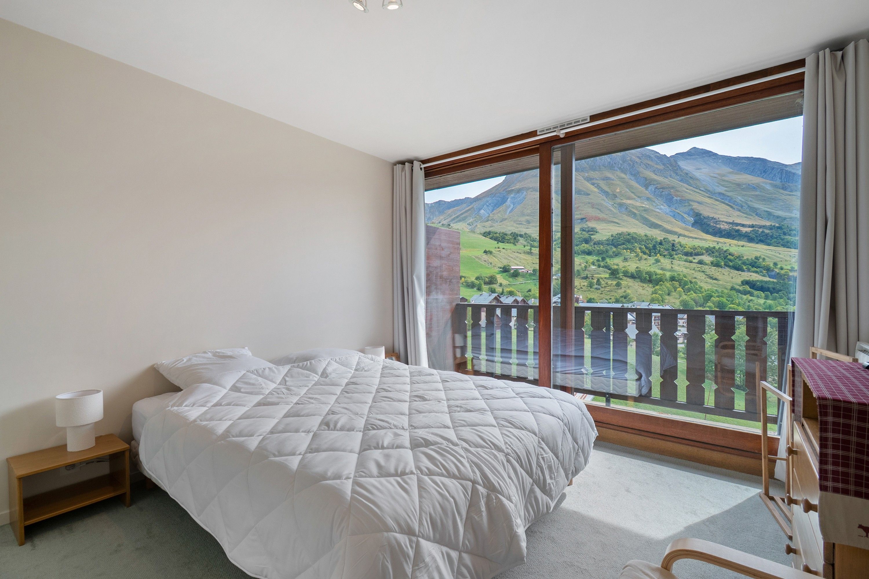 Une chambre avec un grand lit, une table de chevet, une fenêtre donnant sur les montagnes et un balcon avec une balustrade.