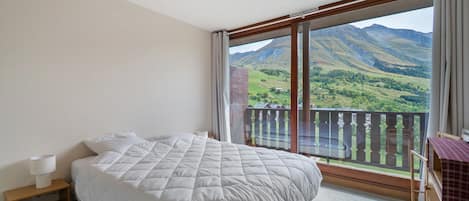 Un dormitorio con una cama grande, una mesita de noche, una ventana con vistas a montañas y un balcón con barandilla.